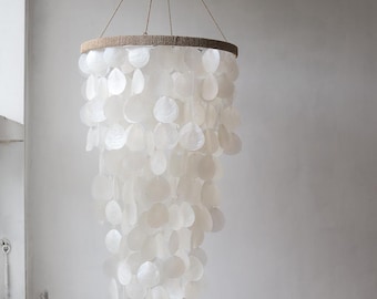 May include: A white capiz shell chandelier with a round, woven top and cascading shell discs. The chandelier hangs from a natural fibre cord, creating a soft, elegant light fixture. The shells are pearlescent and create a shimmering effect.