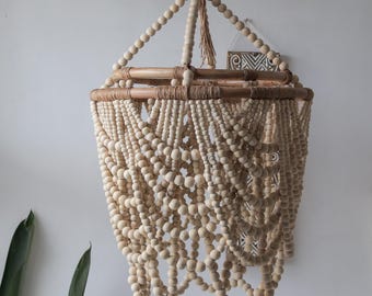 May include: A large, round, wooden bead chandelier with a natural wood finish. The chandelier is made of many strands of beads that are woven together to create a cascading effect. The chandelier is suspended from a single hook.