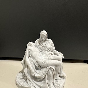 May include: A white 3D printed sculpture of the Pietà, a Renaissance sculpture by Michelangelo, depicting the Virgin Mary holding the body of Jesus Christ.