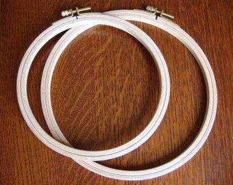 May include: Two wooden embroidery hoops, one inside the other, on a brown wooden surface.