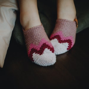 May include: A pair of pink and white crocheted slippers with a pink and red zig-zag pattern.