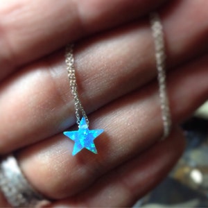 May include: A delicate necklace featuring a small, five-pointed star pendant. The star is a vibrant blue with a shimmering, opal-like effect. The chain is a thin, silver-colored metal, creating a simple and elegant design.
