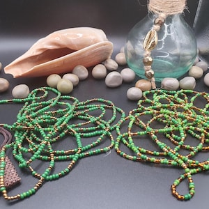 Könnte beinhalten: Zwei grüne und goldene Perlen-Taillenschmuckstücke, auch bekannt als Taillenkette, liegen auf einer schwarzen Oberfläche. Die Perlen bestehen aus kleinen, runden Perlen in Grün- und Goldtönen.