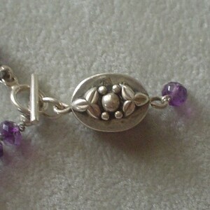 May include: A silver necklace with a decorative clasp and purple amethyst beads.