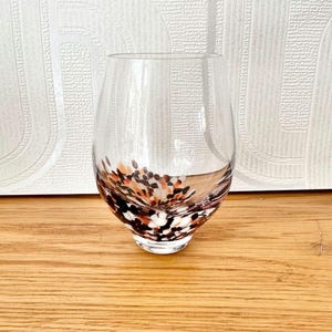 May include: A clear glass with a rounded bottom and a speckled design featuring black, white, and orange spots.