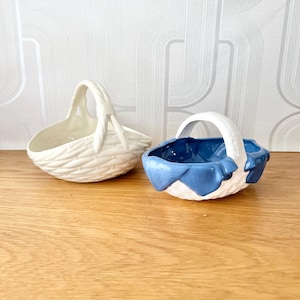 May include: Two white ceramic baskets with woven details. One basket has a blue fabric lining.