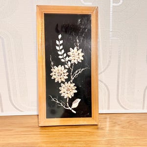Peut inclure: Une œuvre d'art encadrée en bois rectangulaire avec un fond noir et un motif floral. Les fleurs et les feuilles sont blanches et beiges, créant un contraste saisissant. Le cadre est de couleur marron clair.