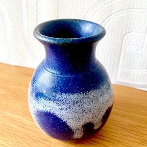 以下が含まれることがあります： 白い斑点と白い釉薬のデザインが施された、小さな青い陶器の花瓶。花瓶は丸い胴体と細い首をしています。