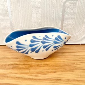 May include: A small, white ceramic bowl with a blue and white floral design. The bowl has a wavy rim and is ideal for holding small items.