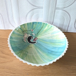 May include: A small, white ceramic bowl with a scalloped edge. The bowl is decorated with a swirling, abstract design in shades of green, blue, and black.