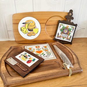 May include: A wooden cheese board with a knife, a small plate with a picture of cheese and crackers, and two small tiles with a cuckoo clock and a floral design.