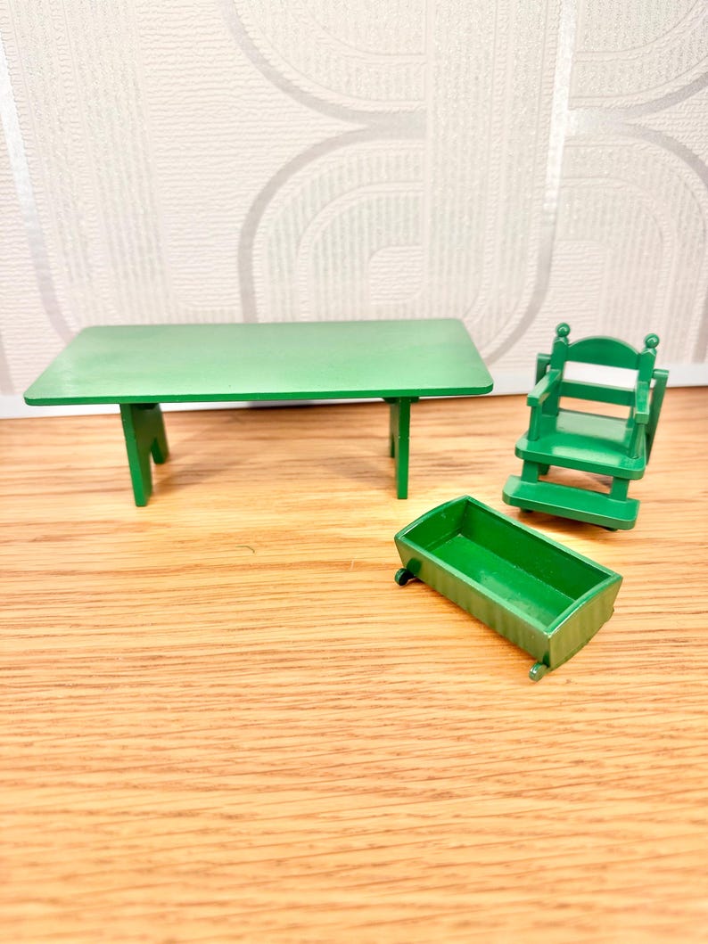 May include: A miniature green furniture set consisting of a rectangular table with four legs, a high-backed chair with armrests, and a small rectangular open-top container. All items are made of solid green plastic with a smooth, uniform finish.