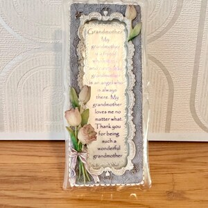 May include: A rectangular decorative plaque with a floral and lace design. The plaque has a silver frame with the words "Grandmother" and a poem about grandmothers. A bouquet of pink and white tulips is attached to the plaque.