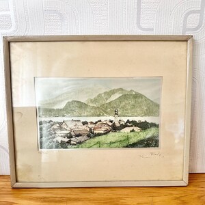 May include: A framed watercolour painting depicting a small village nestled in a valley with a lake and mountains in the background. The painting is signed "K. Roos" in the bottom right corner.