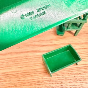 May include: A green plastic toy structure featuring a small rectangular green bin and a staircase component. The structure is embossed with the text 1986 EPOCH TAIWAN. The pieces are molded from solid green plastic with a smooth finish and visible structural details.