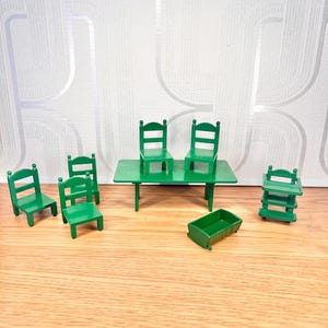 May include: A set of miniature green furniture including a rectangular table, four chairs, a small cradle, and a high chair. Each piece is constructed with a solid green finish and features simple, clean lines typical of dollhouse-scale wooden furniture.