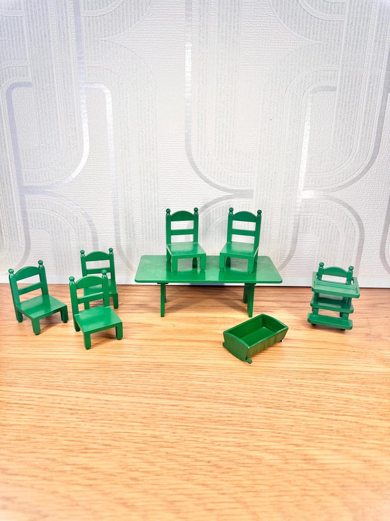 May include: A set of miniature green furniture including a rectangular table, four chairs, a small cradle, and a high chair. Each piece is constructed with a solid green finish and features simple, clean lines typical of dollhouse-scale wooden furniture.