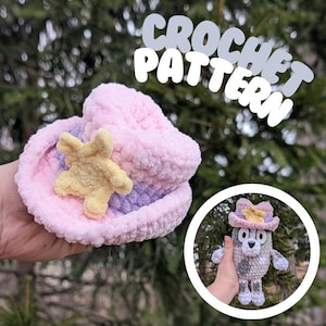 May include: Crochet pattern for a pink and purple cowboy hat with a yellow star. The hat is being held in a hand. The image also shows a crocheted gray dog wearing the same hat.