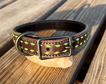 May include: A dark brown leather dog collar featuring bright lime green decorative stitching and lacing. The collar includes a matte black metal buckle and a matching D-ring for leash attachment, with multiple adjustment holes along the strap.