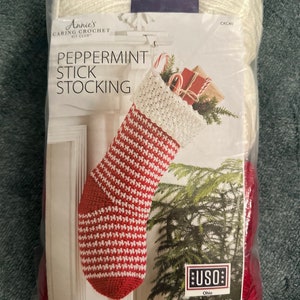 May include: A Peppermint Stick Stocking crochet kit from Annie's Caring Crochet Kit Club. The kit includes red and white yarn and instructions for a Christmas stocking. The packaging features a completed stocking design with candy canes and gifts.