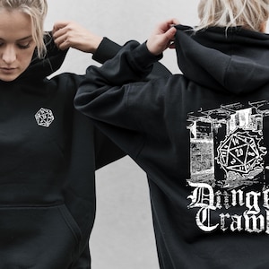 Puede incluir: Sudadera con capucha negra con un bolsillo delantero y un diseño geométrico blanco en el pecho. La parte trasera de la sudadera presenta un gráfico de un dado y las palabras "Dungeon Cramblers" en fuente gótica.