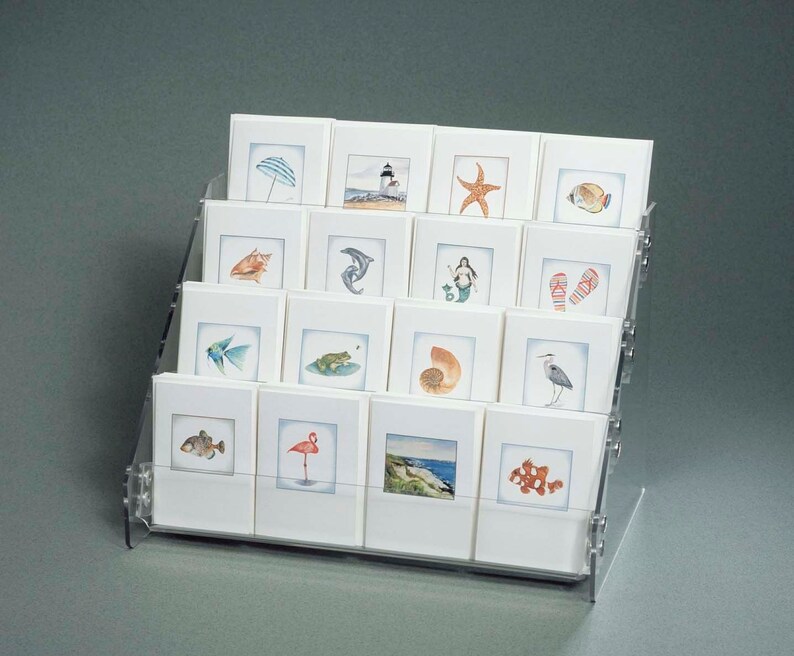 May include: A clear acrylic display stand with 18 white card holders. Each card features a watercolor illustration of a beach-themed image, such as a seashell, starfish, and a lighthouse.