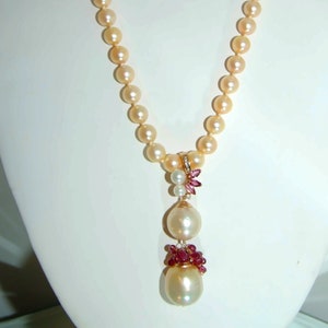 May include: A pearl necklace with a pendant featuring two large pearls and pink gemstones. The necklace is made of cream-colored pearls and the pendant is accented with gold.