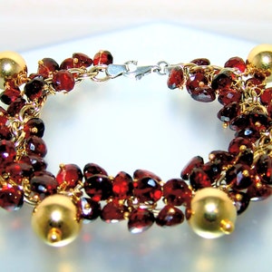 May include: A gold bracelet with a chain and red garnet stones. The bracelet has a clasp closure.