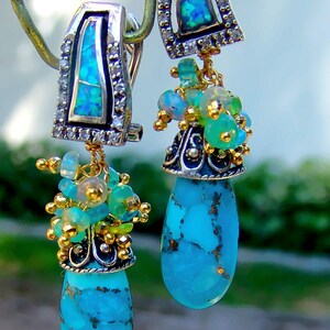 May include: A pair of dangle earrings with turquoise stones and opal accents. The earrings are silver and gold toned and feature a cluster of green and blue gemstones.