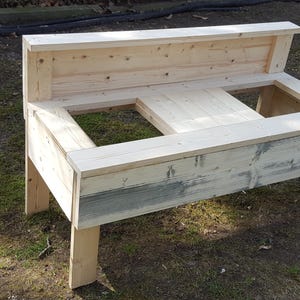 May include: A wooden table with two open compartments and a back panel. The table is made of unfinished wood and has a rustic look.