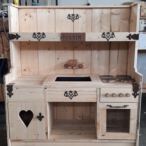 Puede incluir: Una cocina de juguete de madera con un fregadero, una estufa, un horno y armarios. La cocina está pintada de blanco y tiene un letrero que dice "KEUKEN" en la parte superior.