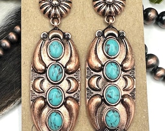 May include: A pair of copper-toned dangle earrings featuring a circular stud top and an elongated oval drop. Each earring is set with four oval turquoise-colored stones with black veining, accented by crescent moon shapes and textured metal details.