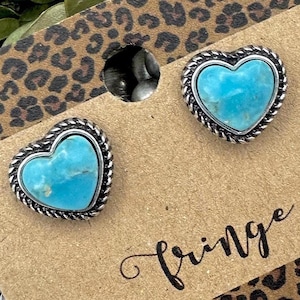 May include: Heart-shaped stud earrings with a turquoise stone center and a silver-colored rope-like border. The earrings are displayed on a brown card with the word "Fringe" in cursive. The background has a leopard print.