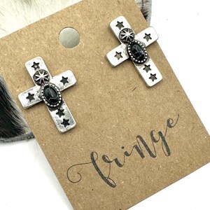 May include: A pair of silver cross earrings with black stones and star accents. The earrings are displayed on a brown card with the word "Fringe" written on it.