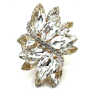May include: A gold-toned ring featuring a cluster of clear, faceted crystals arranged in a floral design. The crystals are elongated and pointed, with a smaller band of clear stones crossing the center.