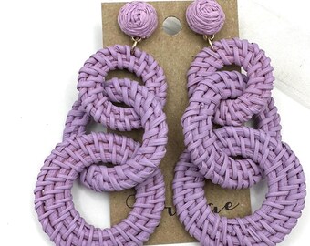 May include: A pair of lavender woven circle earrings. The earrings are made of three woven circles, each with a different diameter. The earrings are a statement piece and would be perfect for a summer party or a night out.