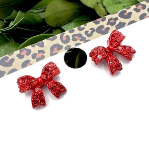 May include: A pair of red rhinestone bow earrings on a white card with the word "fringe" written in black cursive.