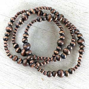 May include: Three copper-toned beaded bracelets with a layered look. The beads are round and have a slightly textured surface.