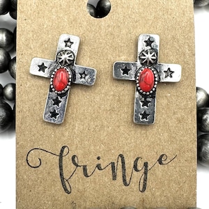 May include: A pair of silver cross earrings with red stone accents and star details. The earrings are displayed on a brown card with the word "fringe" written on it.