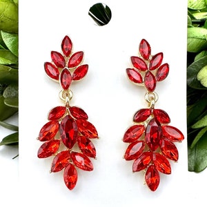 May include: A pair of dangle earrings with a gold tone setting and red crystal accents. The earrings feature a cluster of red crystals in a teardrop shape.