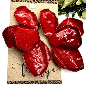 May include: Red petal-shaped earrings with a glossy finish. The earrings are attached to a brown card with a leopard print border and the word "fringe" in cursive. Green leaves are in the background.