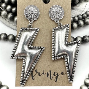 May include: Silver lightning bolt earrings with a decorative floral design at the top. The earrings are displayed on a brown card with the word "Fringe" written on it.