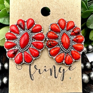 May include: A pair of red and silver earrings with a floral design. The earrings are made of metal and have a red stone in the center. The earrings are on a brown background with the word "fringe" written on it.