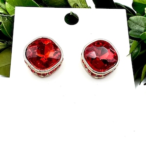 May include: A pair of red square-shaped earrings with a silver setting and small red crystals around the edge.