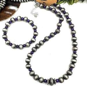 May include: A silver-toned necklace and bracelet set with purple accents. The necklace and bracelet feature large, round beads interspersed with smaller purple beads. A brown tag with the word "Fringe" is visible.