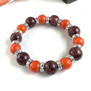 May include: A stretch bracelet with alternating red and maroon beads. Each bead is accented with clear rhinestones.