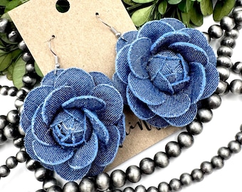May include: A pair of denim flower earrings with a blue color. The earrings are made of fabric and have a simple design.