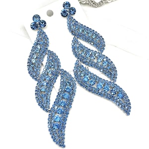 May include: A pair of dazzling blue rhinestone earrings. Each earring features a cluster of three small rhinestones at the top, with a flowing, leaf-like design of larger rhinestones cascading downwards. The earrings are set against a white background.
