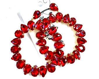 May include: A pair of red teardrop-shaped earrings with gold-colored metal accents. The earrings are arranged in a circular pattern, with each teardrop gem closely set together. The gems are a vibrant red color, and the earrings are set against a white background.