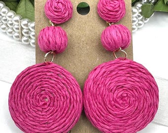 May include: A pair of pink paper earrings with a large round, spiral design. The earrings have three smaller round paper balls on each earring.